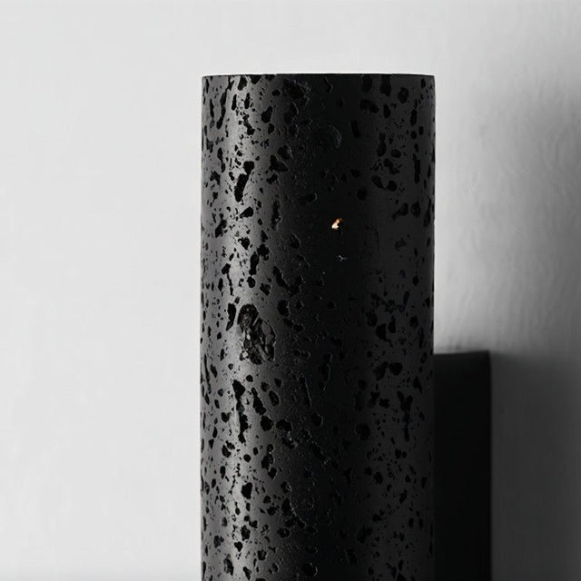 "Close-up of a black travertine cylindrical wall lamp showing its textured surface."