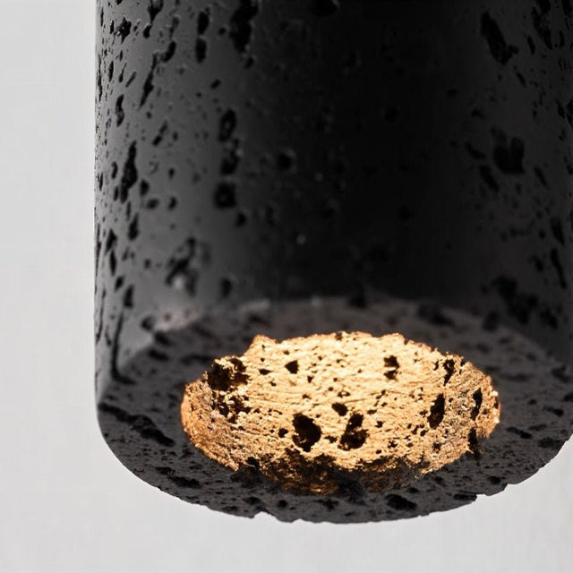 "Close-up of a black travertine cylindrical wall lamp showing the textured surface and the light source detail at the bottom."