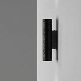 "Side view of a black travertine cylindrical wall lamp mounted on a light wall."