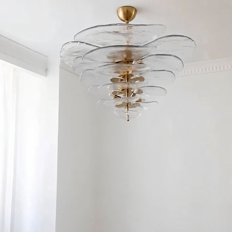 "A clear Murano glass chandelier with layered petals, hanging in a room with white walls and a curtain."