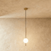 Brass pendant light with white frosted glass sphere, hanging above bedside table in modern bedroom setting.