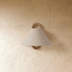 Modern wall sconce with curved brass arm and tapered gray linen shade on white studio background, angled view.