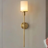 "A tall, elegant brass wall lamp with a cylindrical alabaster shade casting a warm glow on a neutral wall."