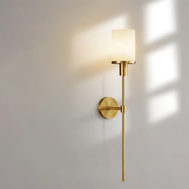 "A minimalist brass wall lamp with a cylindrical alabaster shade, casting a warm, soft light on a neutral wall with a subtle shadow."