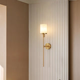 "A minimalist brass wall lamp with a cylindrical alabaster shade casting a warm glow on a textured white wall."