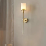 "A minimalist brass wall lamp with a cylindrical alabaster shade casting a warm, ambient glow in a modern living room."