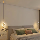 "Two gold pendant lights with a spiral design, shown lit up on either side of a bed with pillows and a throw blanket."