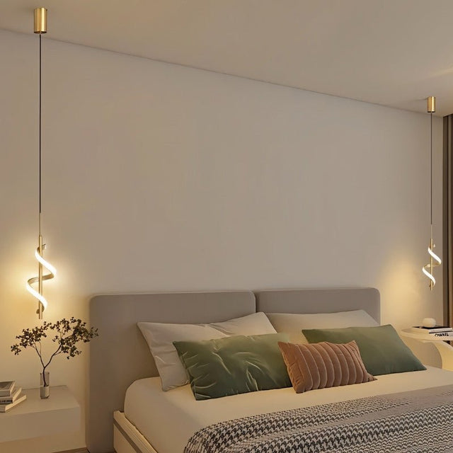 "Two gold pendant lights with a spiral design, shown lit up on either side of a bed with pillows and a throw blanket."