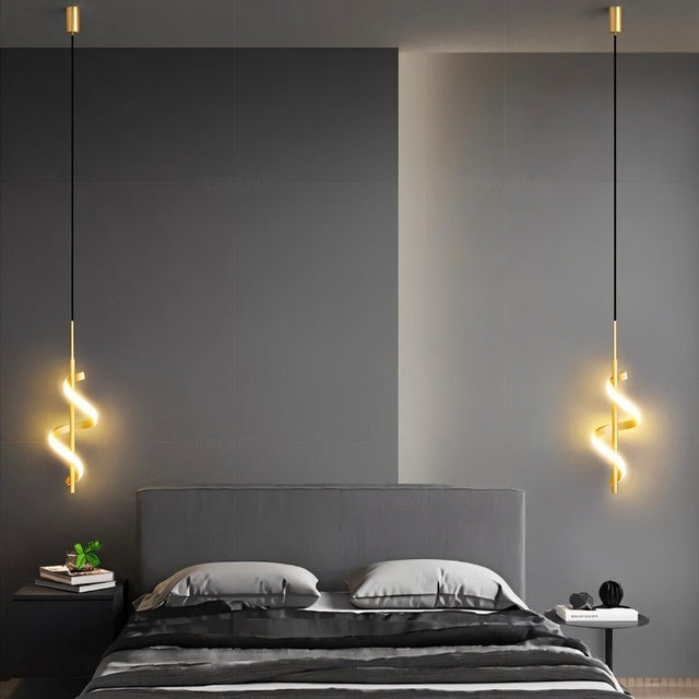 "Two gold pendant lights with a spiral design, shown lit up on either side of a bed with gray bedding and a gray headboard, in a room with dark gray and light gray walls."