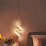 "A gold pendant light with a spiral design, shown lit up in a bedroom with a plant, a book, and a bed."
