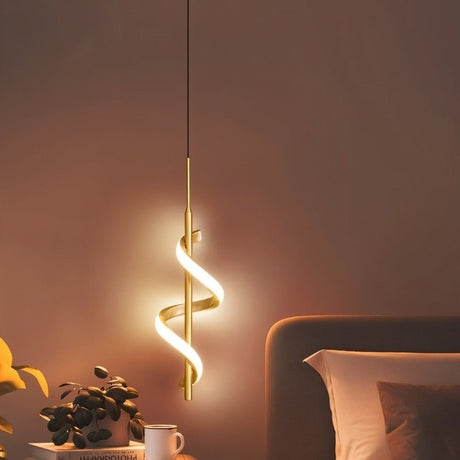 "A gold pendant light with a spiral design, shown lit up in a bedroom with a plant, a book, and a bed."