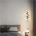 Wall-mounted lamp with a spiral design, featuring a sleek metal finish, illuminating a cozy bedroom setting.
