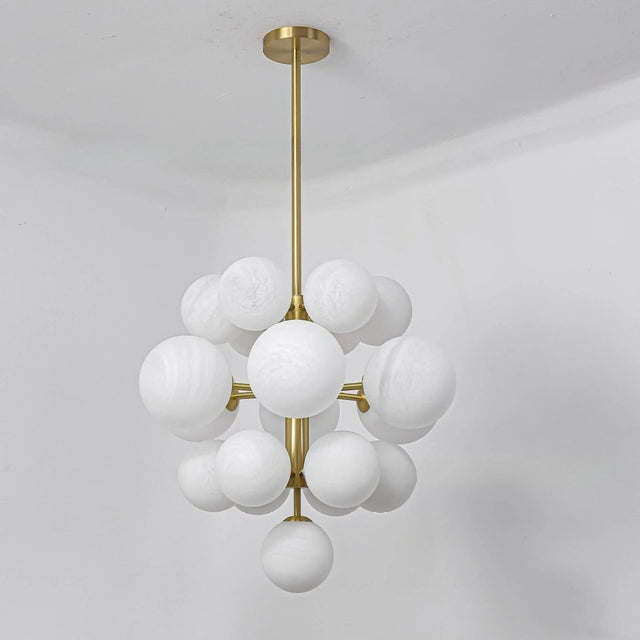 "A modern brass chandelier with a sculptural design, featuring frosted glass globes clustered around a central rod."