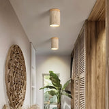 "Two cylindrical yellow travertine ceiling lights with light wood bases in a hallway with wooden accents, modern interior lighting."