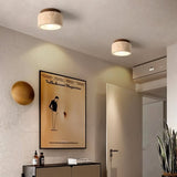 "Two cylindrical yellow travertine ceiling lights with dark wood tops in a hallway with artwork, modern interior lighting."