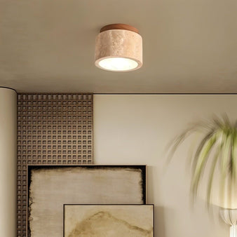 "Cylindrical yellow travertine ceiling light with dark wood top in a room with textured walls and artwork, modern lighting."