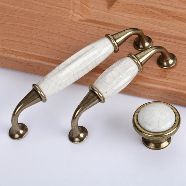 "Ceramic pull bar handles with a crackled glaze and zinc alloy supports, alongside a matching knob, in an antique brass finish."