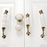 "Ceramic pull bar handles and matching knobs with a crackled glaze and antique brass finish on white shaker-style cabinet doors."