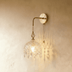 Brass pendant lamp with crystal beaded dome shade hanging from curved arm mount against white studio background