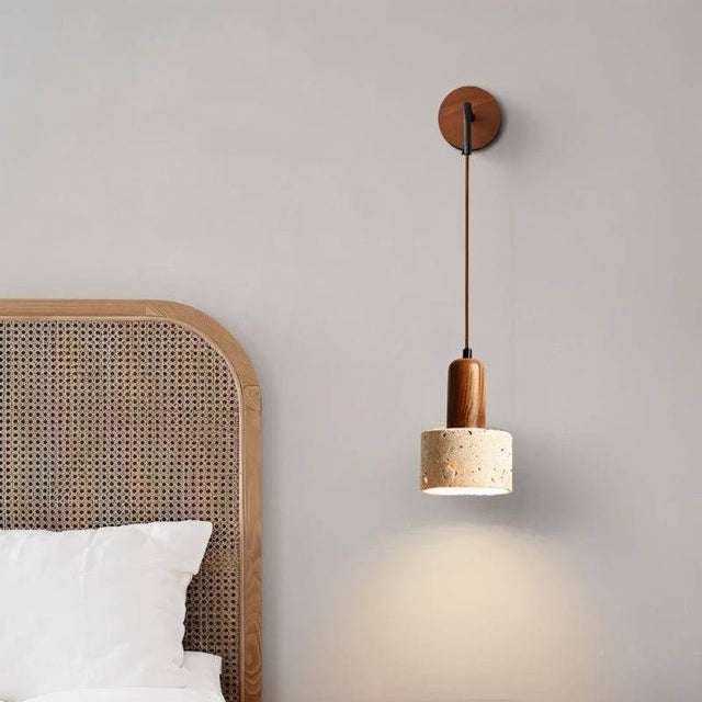 "A modern wall lamp with a cylindrical yellow travertine shade and a wooden mount, casting a soft, downward light in a bedroom setting."
