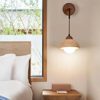 "A modern wall lamp with a dome-shaped yellow travertine shade and a wooden mount, casting a warm, ambient light in a bedroom setting."