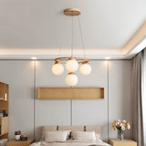 "Circular wood frame chandelier with four frosted glass globes hanging above a bed in a modern bedroom."