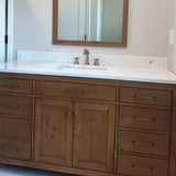 "Minimalist antique brass pull bar handles on a rustic wood bathroom vanity with a white countertop and a mirror above."