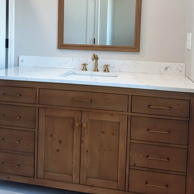 "Minimalist antique brass pull bar handles on a rustic wood bathroom vanity with a white countertop and a mirror above."