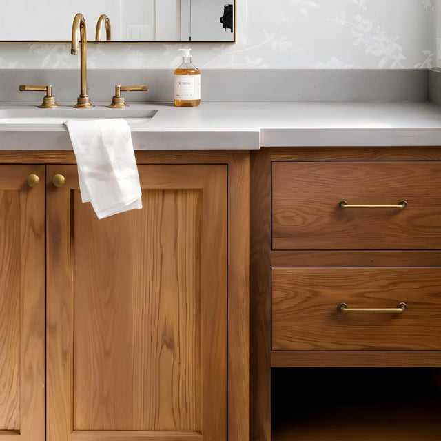 "Minimalist antique brass pull bar handles on drawers and knobs on cabinet doors in a modern bathroom with a white countertop and a faucet."