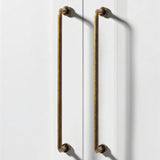 "Two long, minimalist antique brass pull bar handles made of durable zinc, installed on white doors, featuring a slim, cylindrical design with rounded ends."