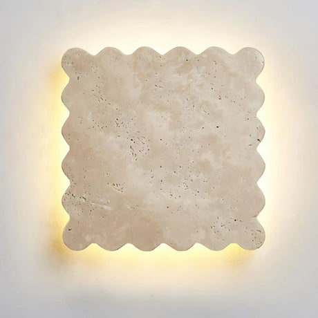 "Close-up of the square Amon travertine wall lamp, showcasing its distinctive scalloped edges and the natural variations in the travertine stone, illuminated from behind with a soft, warm light."