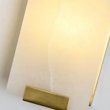 "Close-up of a rectangular alabaster panel on a modern wall lamp, showing its texture and the soft, warm light it emits, with a brass accent at the bottom."