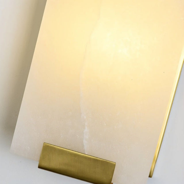 "Close-up of a rectangular alabaster panel on a modern wall lamp, showing its texture and the soft, warm light it emits, with a brass accent at the bottom."
