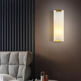 "A modern wall lamp with a rectangular alabaster panel and brass accents, providing a soft, ambient glow in a contemporary bedroom."