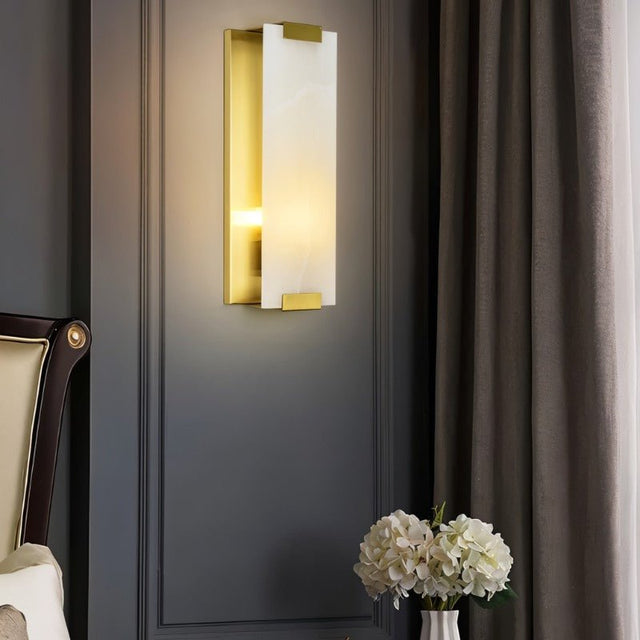 "A modern wall lamp with a rectangular alabaster panel and brass accents, providing a soft, ambient glow in a contemporary living room."