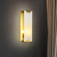 "A modern wall sconce featuring a rectangular alabaster panel illuminated from within, framed by brass accents, mounted on a dark gray wall."