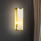 "A modern wall sconce featuring a rectangular alabaster panel illuminated from within, framed by brass accents, mounted on a dark gray wall."