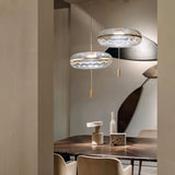 "Two sculptural glass pendant lights with rippled texture and metal frames, hanging above a dining table with decorative items."