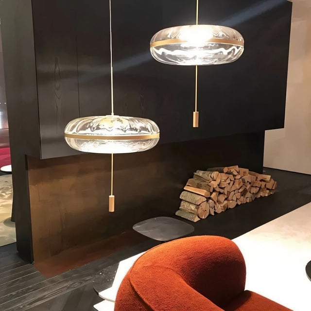 "Two sculptural glass pendant lights with rippled texture and metal frames, hanging in a living room with firewood and a fireplace."