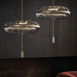 "Pair of sculptural glass pendant lights with rippled texture and metal frames, hanging in a room with dark walls."