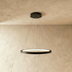 Three curved white LED pendant lights suspended above a black table in a modern interior with textured gray wall.