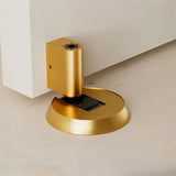 "Gold brass door stop installed on a floor next to a white door."
