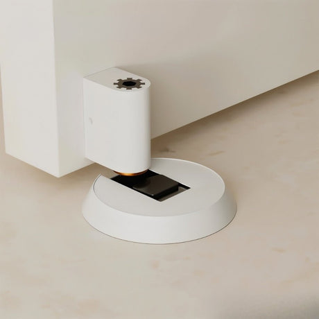 "White brass door stop installed on a floor next to a white door."