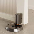 "Brushed brass door stop installed in a modern home setting, next to a white door and light-colored flooring."