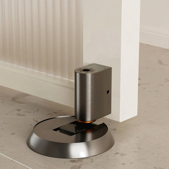 "Brushed brass door stop installed in a modern home setting, next to a white door and light-colored flooring."