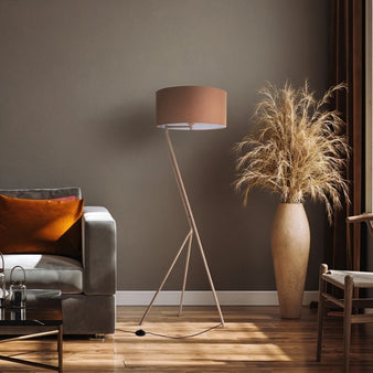 "Anubi floor lamp with an apricot fabric shade and slender stand in a modern living room setting with a gray sofa and large vase."