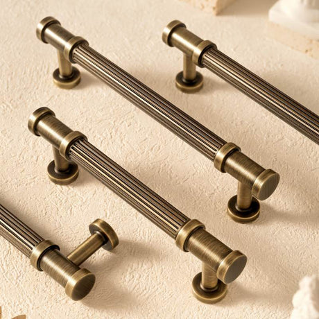"Antique brass fluted cabinet knobs and pull bars with detailed end caps, adding classical charm to vintage and modern interiors."