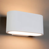 "White gypsum Arcat wall lamp with a rounded rectangular shape, emitting soft uplighting and downlighting on a gray wall."