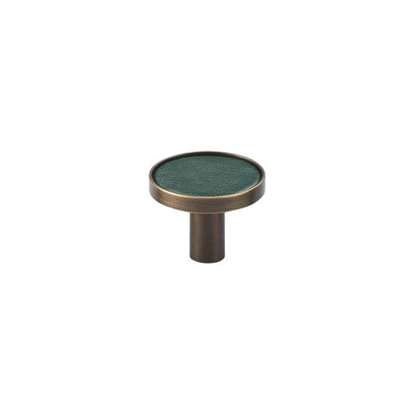 "A modern green leather and brass cabinet knob on a white background."
