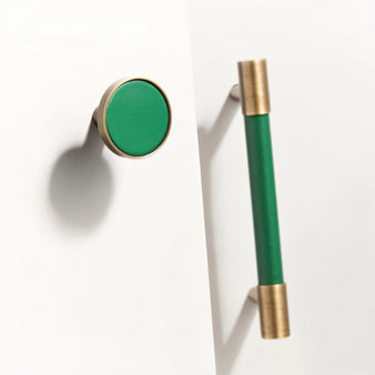 "Modern green leather and brass cabinet knob and pull bar on a white background."